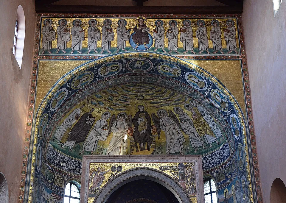 The apse of a church covered in gold-ground mosaics, a row of standing apostles above an arch framed with round portrait medallions, and in the semi-dome below the Virgin enthroned with the Child between saints and angels.