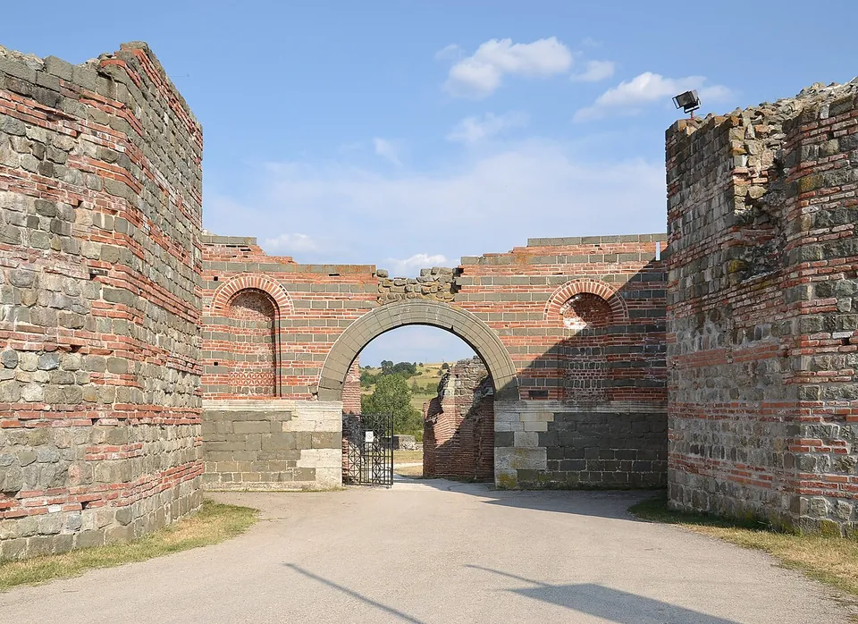 A round-headed brick arch in the circuit wall, flanked by two massive towers of grey stone banded with courses of red brick, with a gravel track running out through the opening.