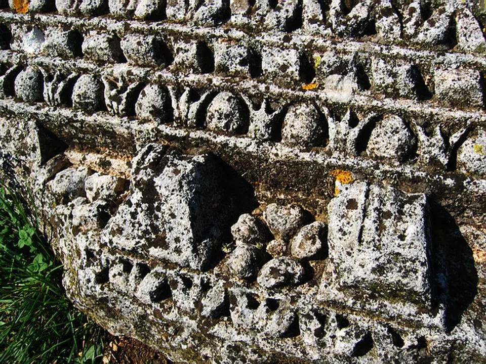 Close view of a weathered limestone cornice block carved with a row of egg-and-dart moulding and square dentils, lying in the grass.