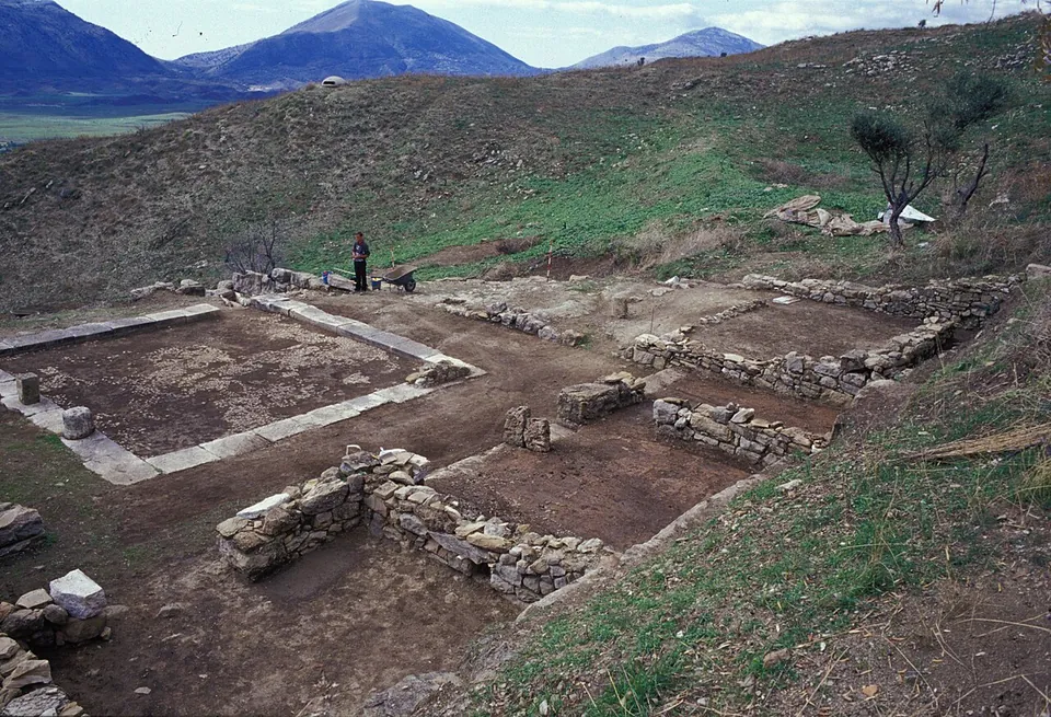 The excavated foundations of a courtyard house on a hillside, a square court edged with stone, with walls of rooms around it.