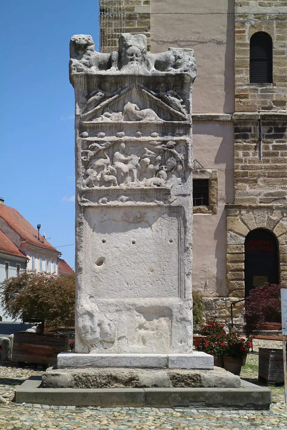 The same stele seen close and square on, its upper panels carved with figures and animals, the lower half plain stone pierced by several round holes, standing on a stepped stone base.