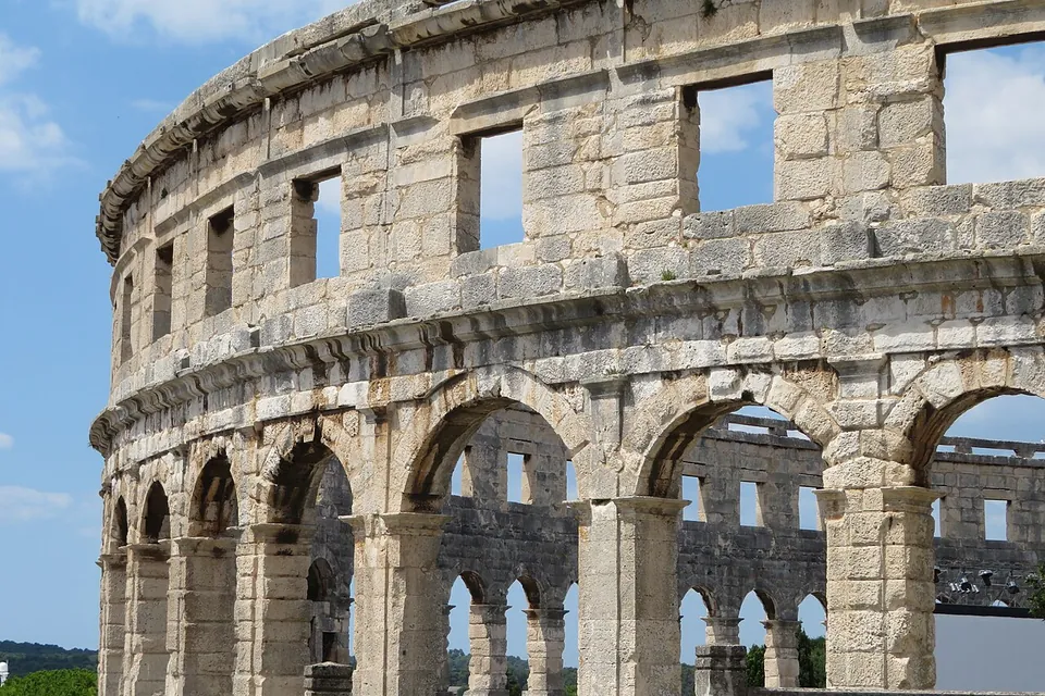 Close view of the upper storeys of the outer wall, large squared limestone blocks forming round arches below and a row of rectangular windows above, with the far side of the wall visible through the openings.