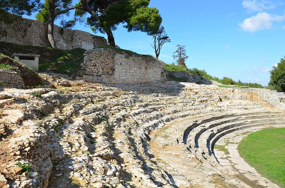 Close view of worn limestone seating rows curving round the edge of a lawn, the stone rough and broken where the rows meet the rock of the slope.
