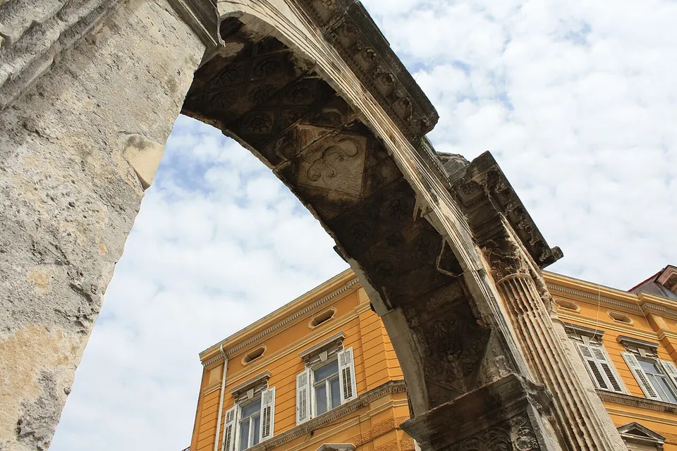 Looking up at the underside of the arch, a coffered stone vault carved with small panels, against a pale sky and the upper floors of a yellow building.